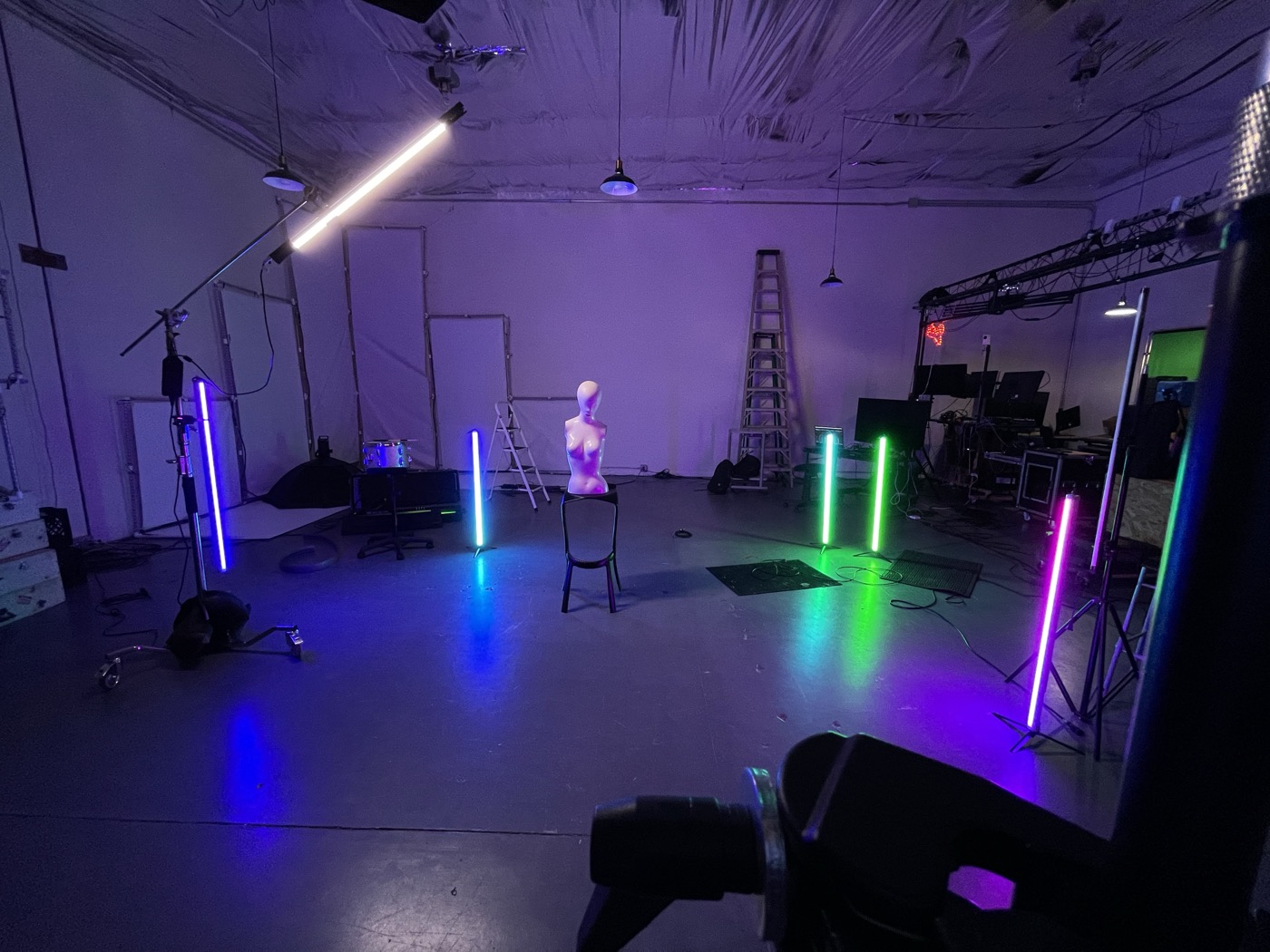 An empty studio before an event, with standing light tubes, screens, overhead metal framing, and ladders in place.