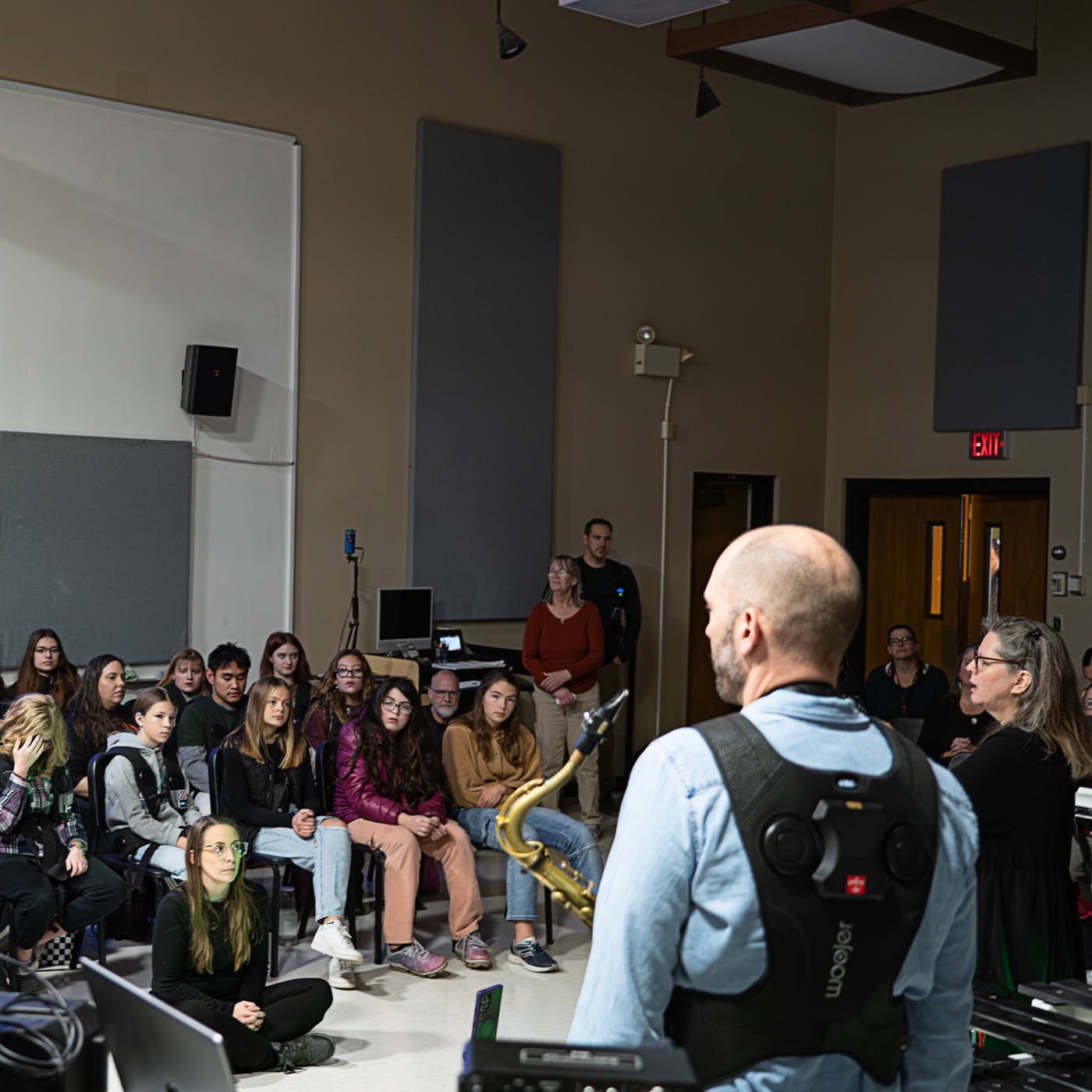 A view from the demonstration area out across the seated Southern Oregon University audience, with a saxophone player in a haptic vest in the foreground and an ASL interpreter at the right.