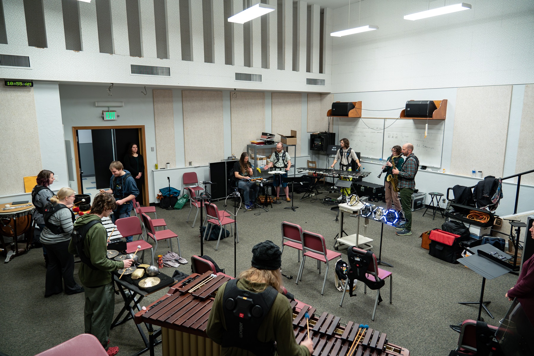 A university percussion room mid-workshop, musicians at mallet instruments and gongs, haptic vests over the chairs.